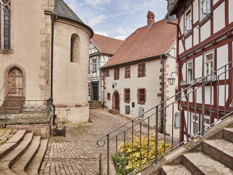 Schlitzer Stadtkirche mit runder Apsis; Blick über eine Treppe auf den Kopfsteinpflaster-Kirchplatz, umgeben von restaurierten Fachwerkhäusern.